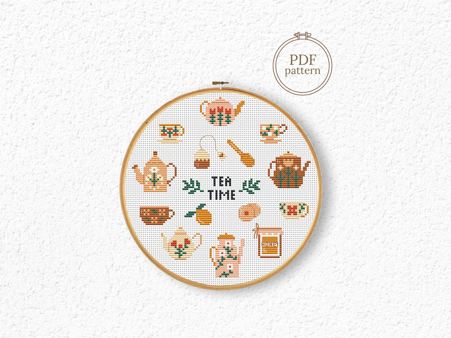 Cross-stitched pattern with tea-themed designs in a hoop on a white background