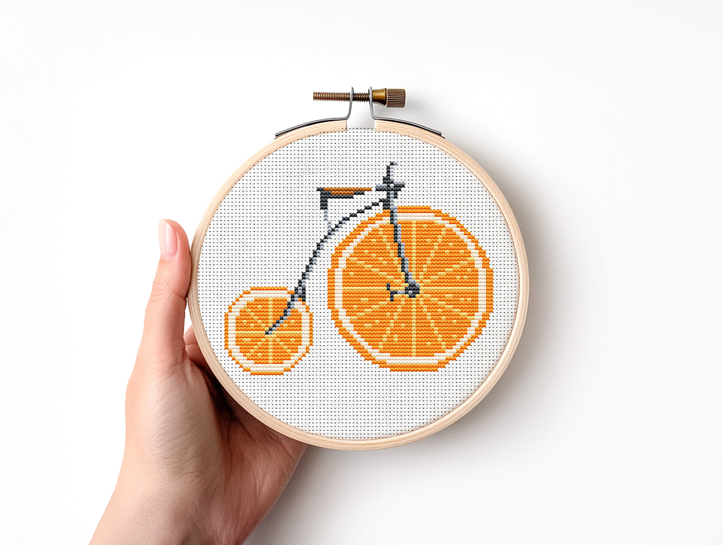 Embroidery hoop with a bicycle design made of orange slices held by a hand on a white background