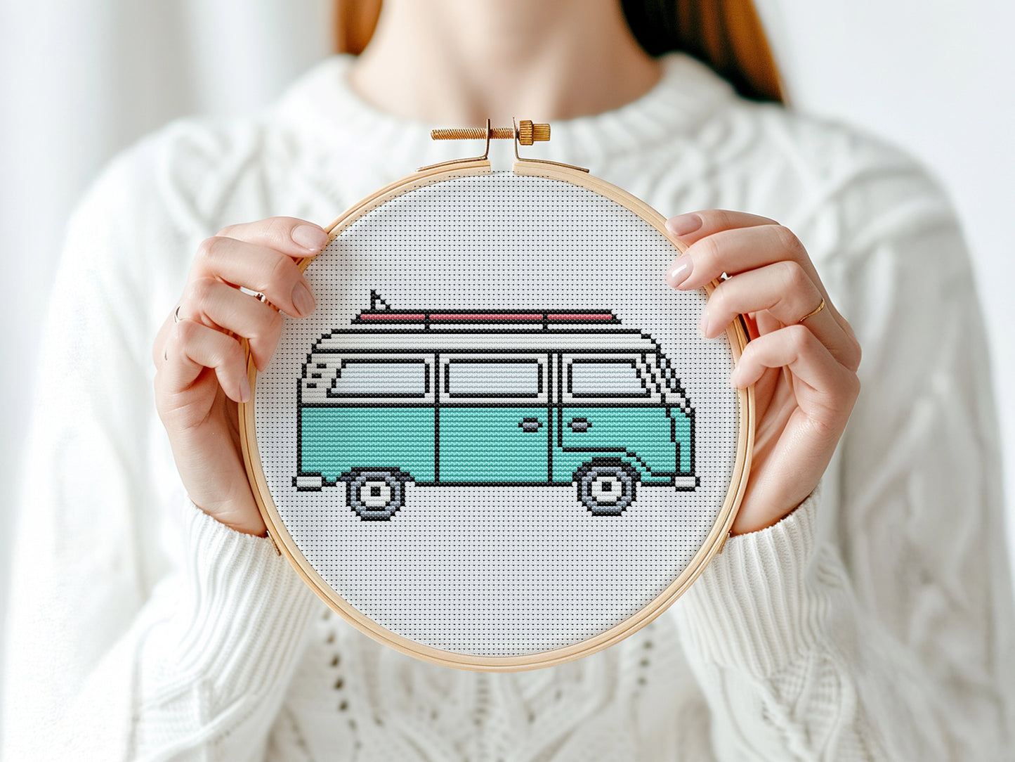 Person holding a cross-stitched design of a van in an embroidery hoop.