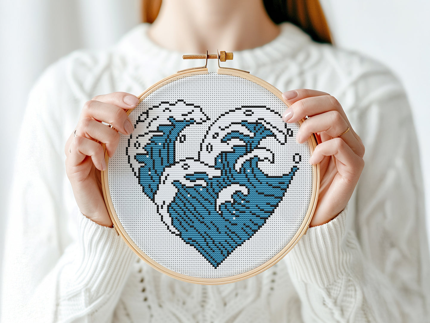 Person holding a cross-stitched heart with wave design in an embroidery hoop.