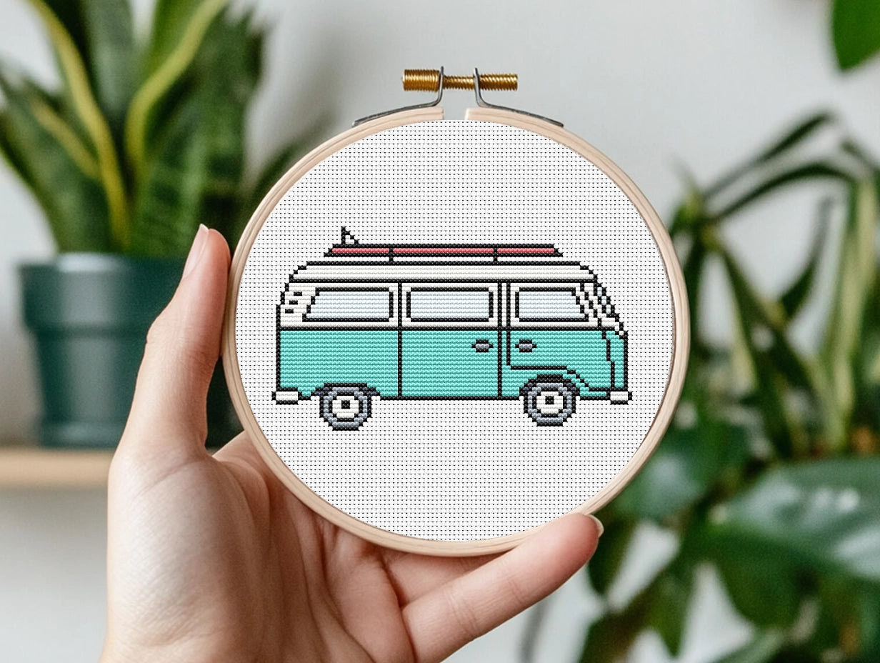 Hand holding a cross-stitched hoop with a vintage van design against a plant background