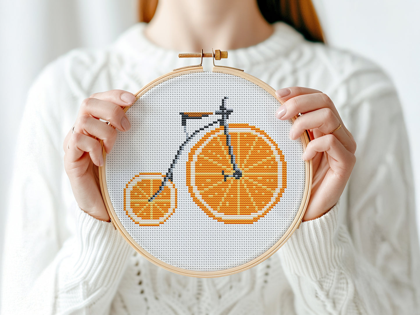 Person holding a cross-stitched bicycle design on fabric with an orange theme.