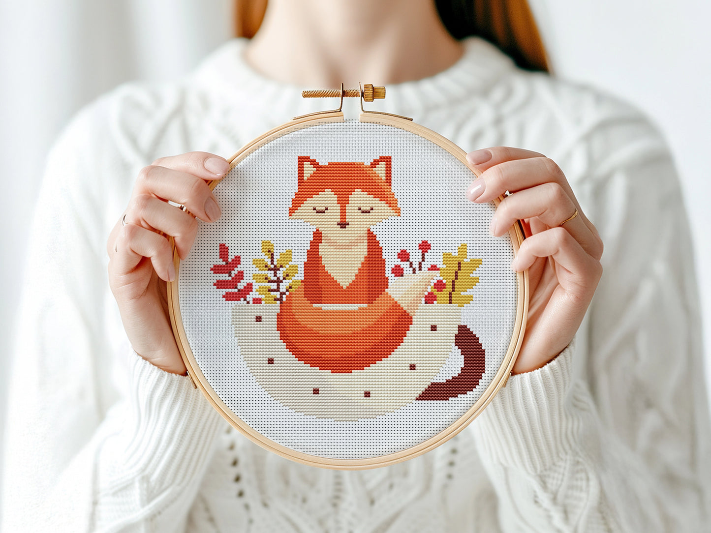 Person holding a cross-stitched hoop with a fox design against a white background