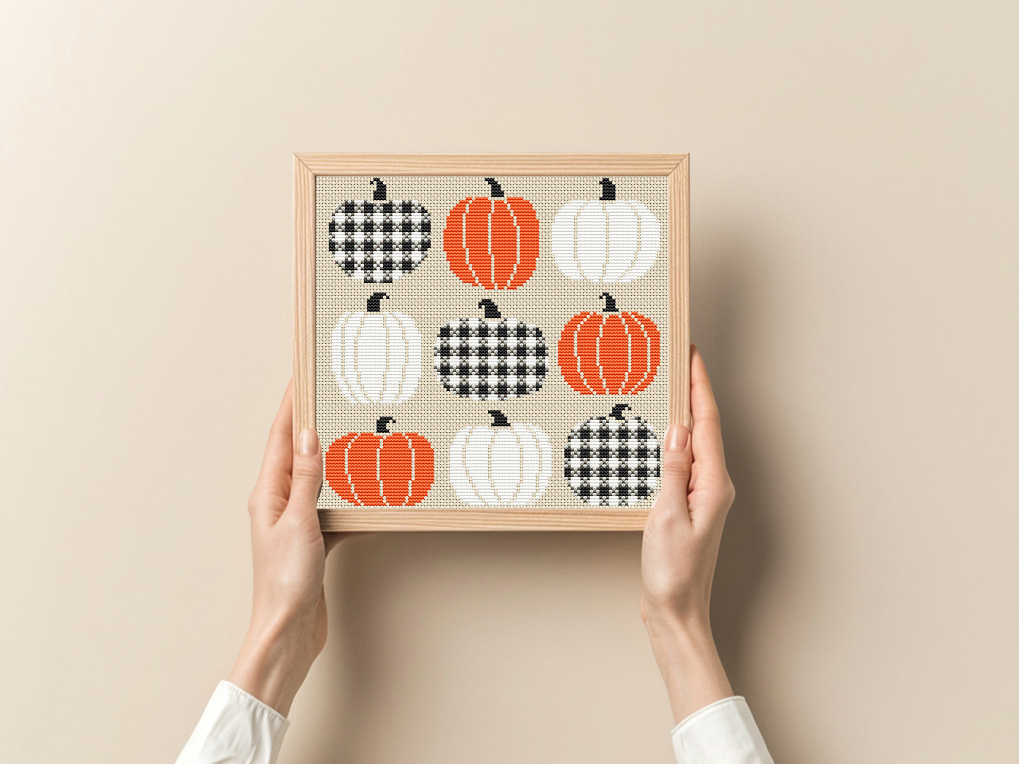 Framed art print with pumpkins and houndstooth patterns held by hands against a beige background