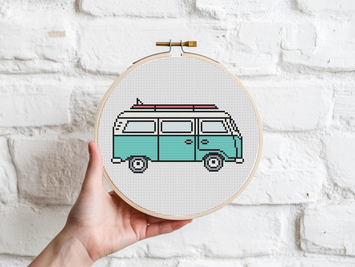 Cross-stitched design of a van held in an embroidery hoop against a white brick wall.