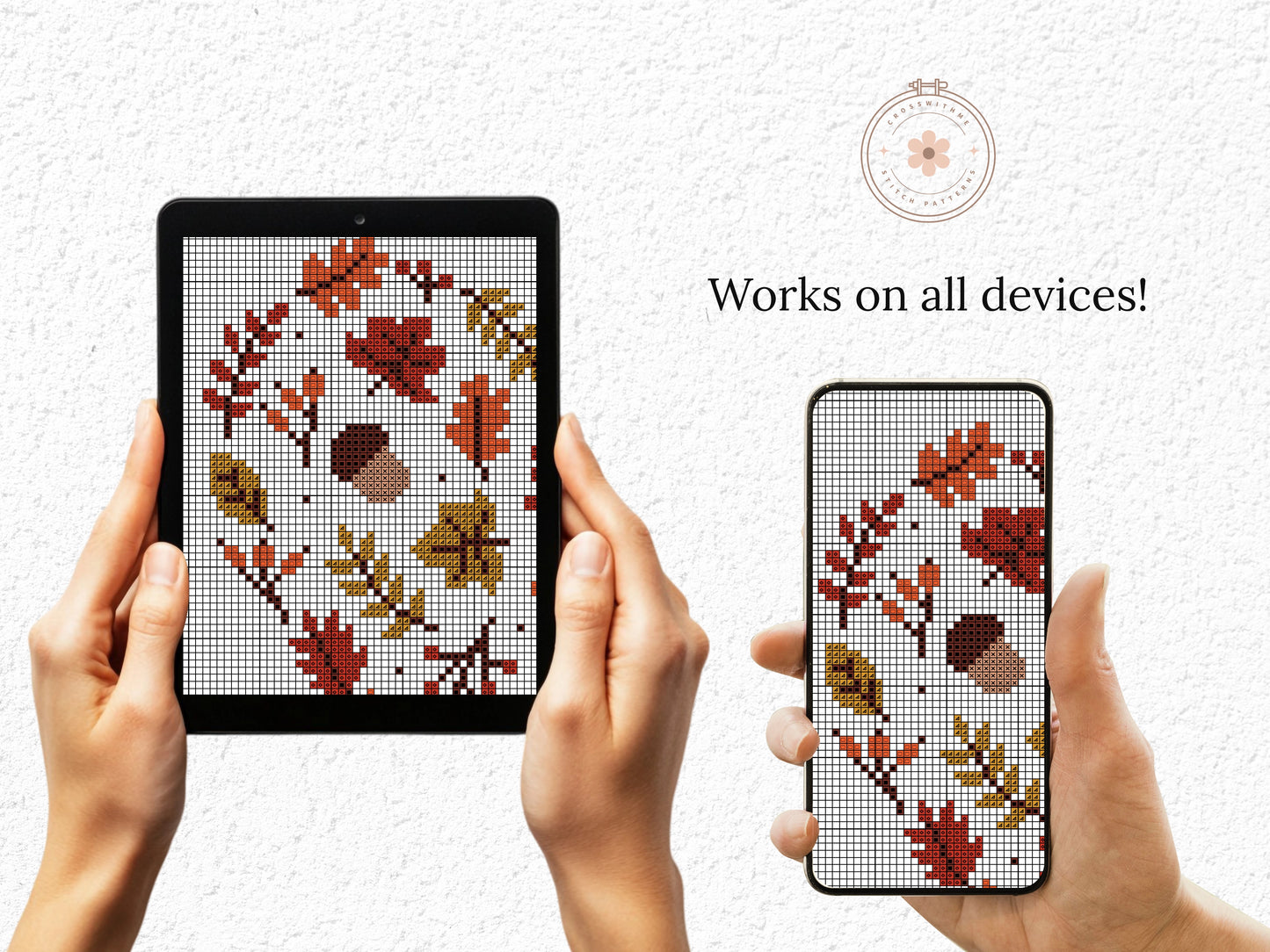 Hands holding a tablet and phone displaying cross-stitch patterns of leaves and acorns.