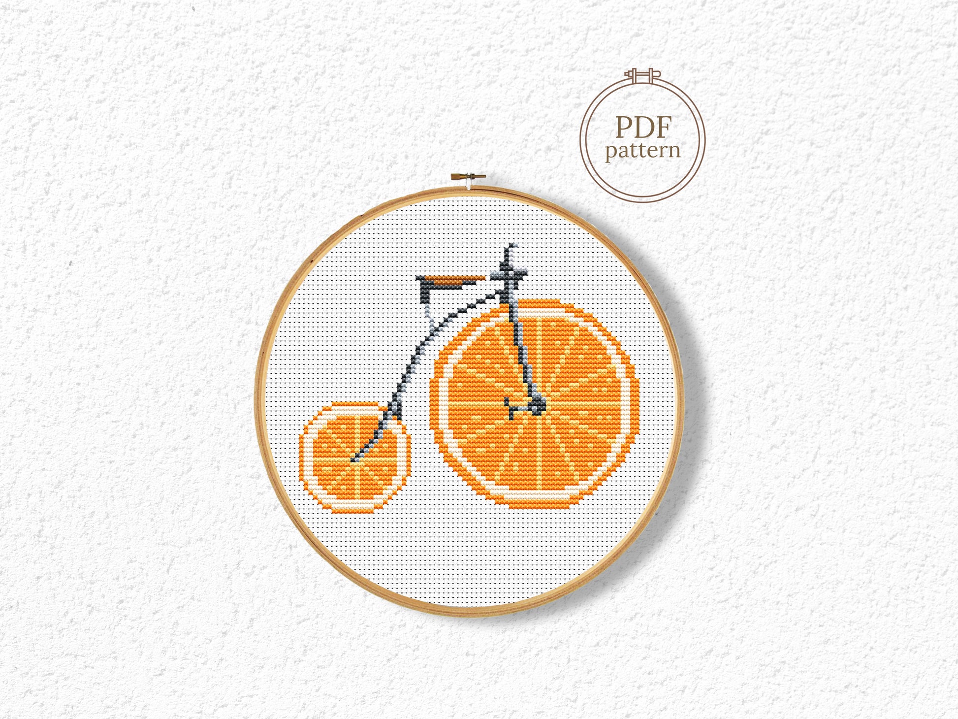 Cross-stitch pattern of a bicycle made from orange slices in an embroidery hoop on a white background.