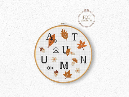 Cross-stitched hoop with 'AUTUMN' text and leaf patterns on a textured white background