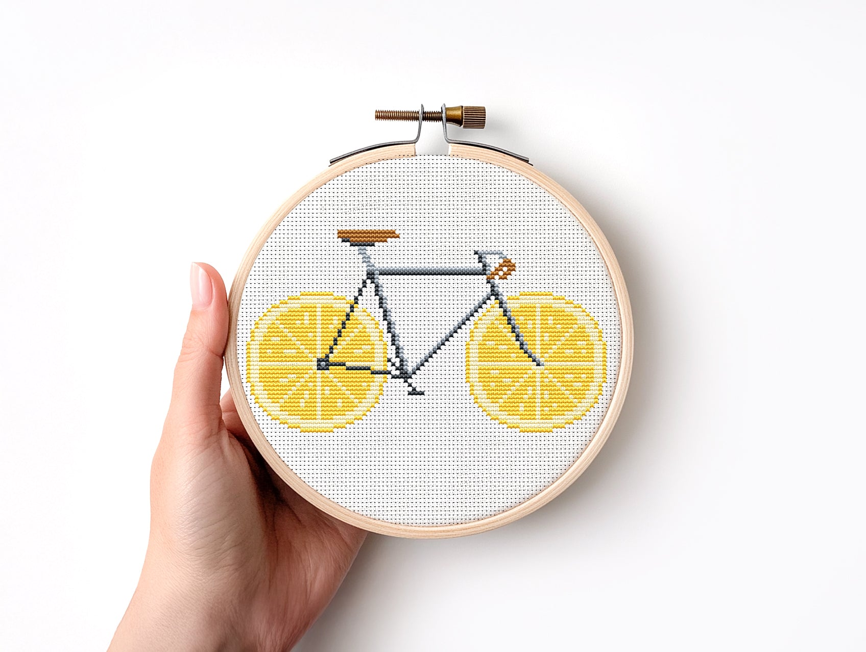 Embroidery hoop with a bicycle design between two lemon slices on a white background