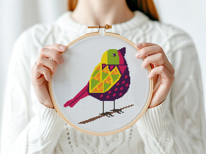 Person holding a cross-stitched hoop with a colorful bird design against a white background