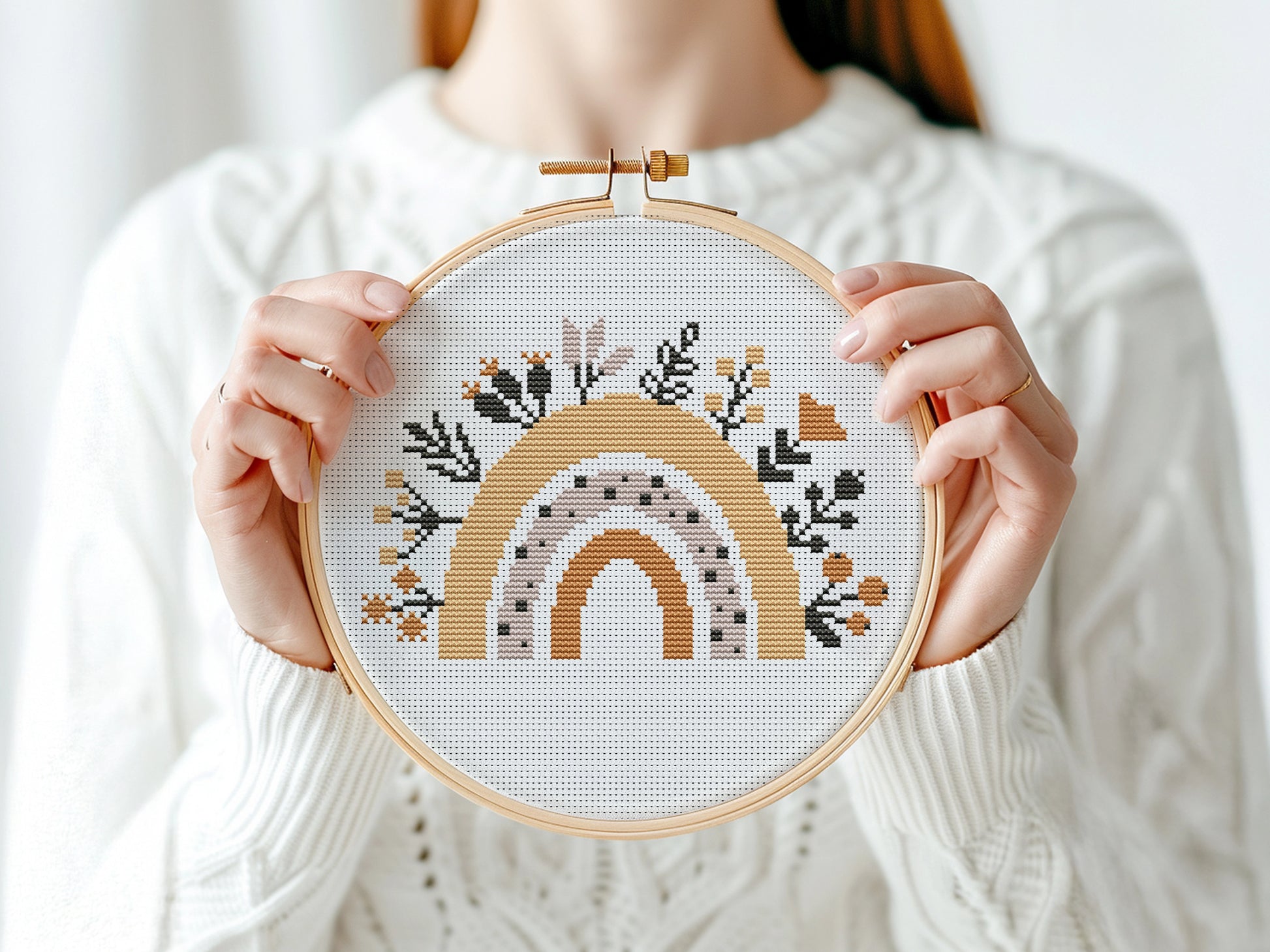 Person holding a cross-stitched hoop with a rainbow design against a white background