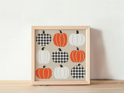 Framed cross-stitch art with pumpkins on a beige background