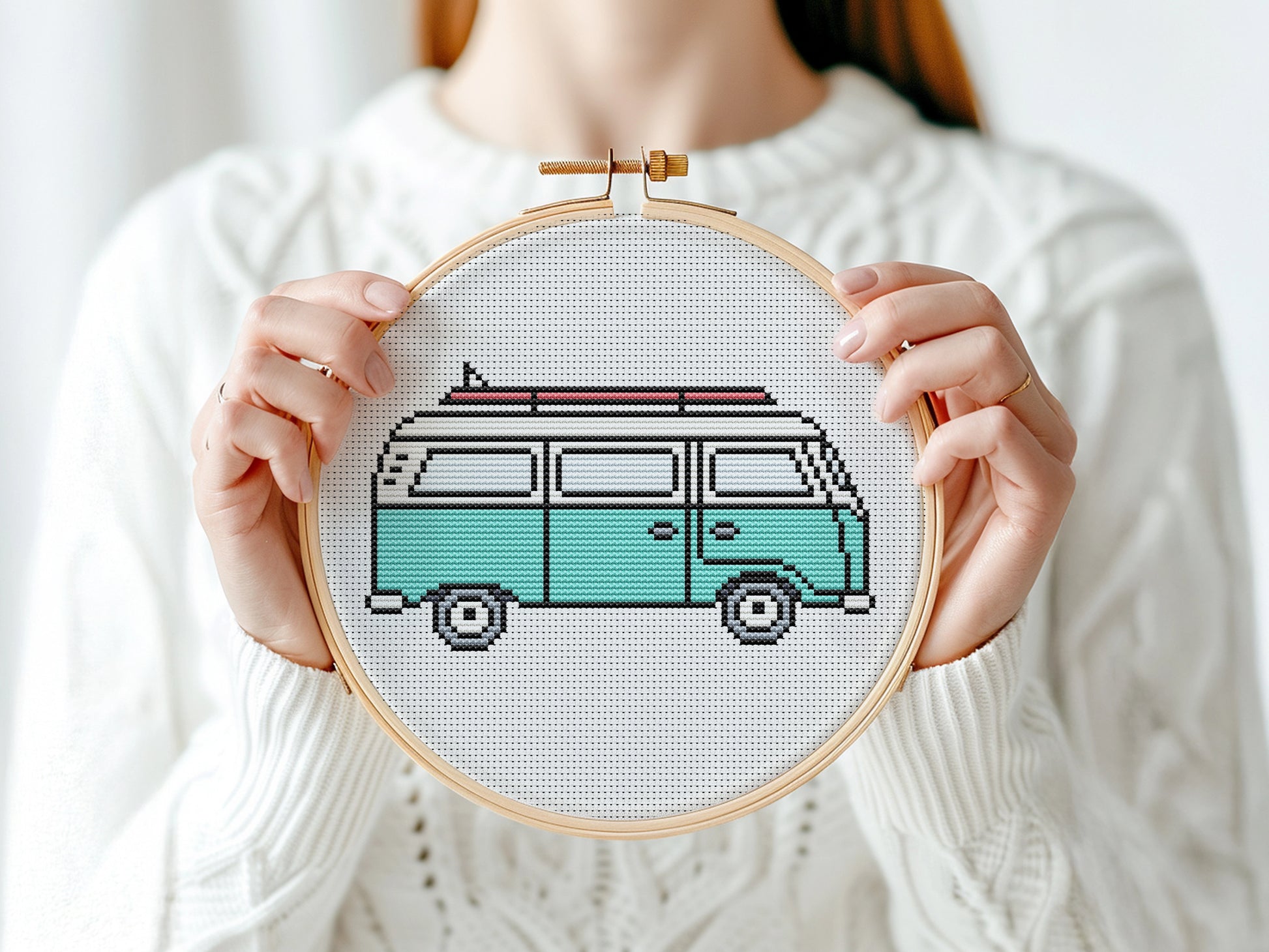 Person holding a cross-stitched design of a van in an embroidery hoop.