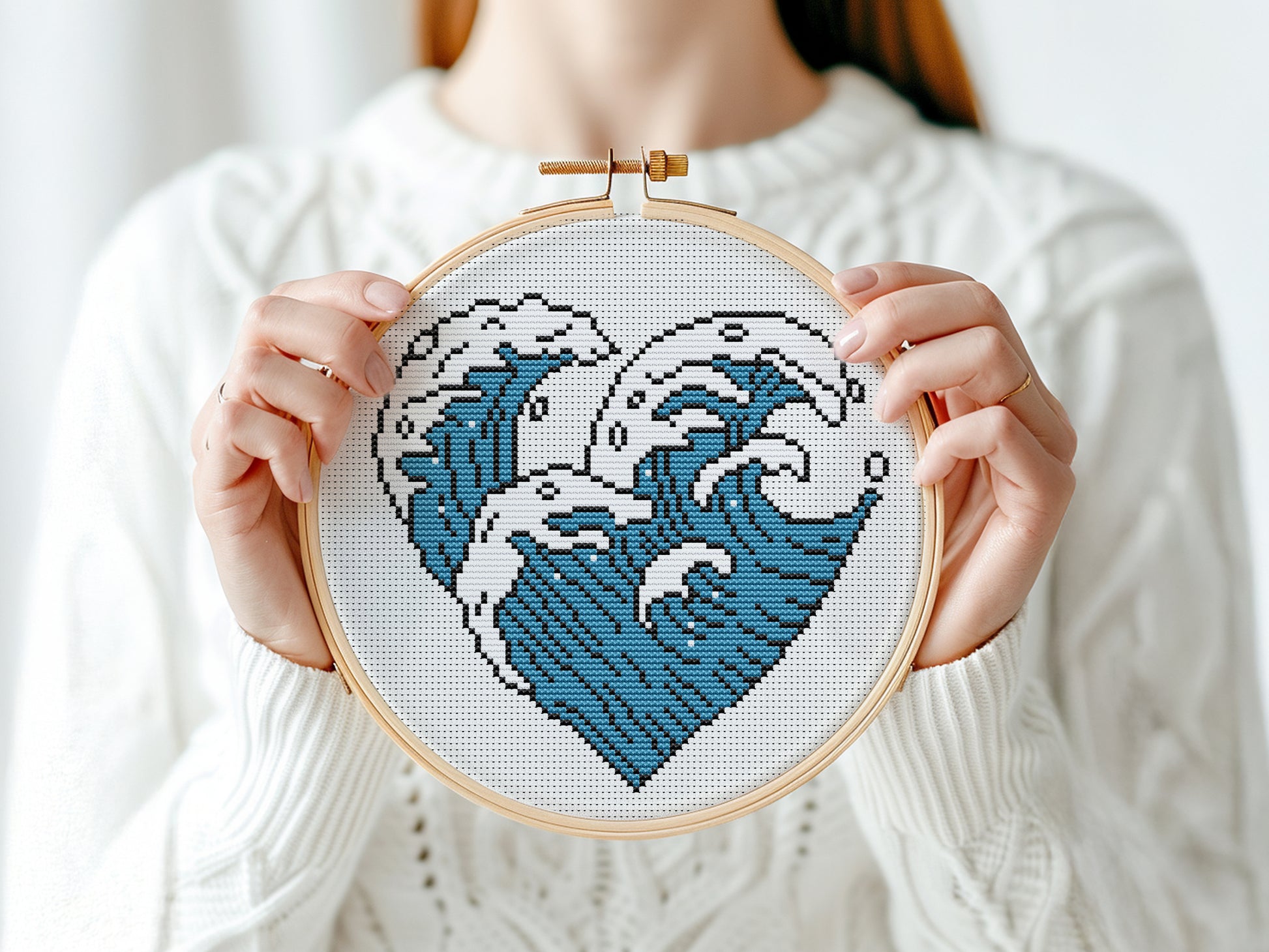 Person holding a cross-stitched heart with wave design in an embroidery hoop.