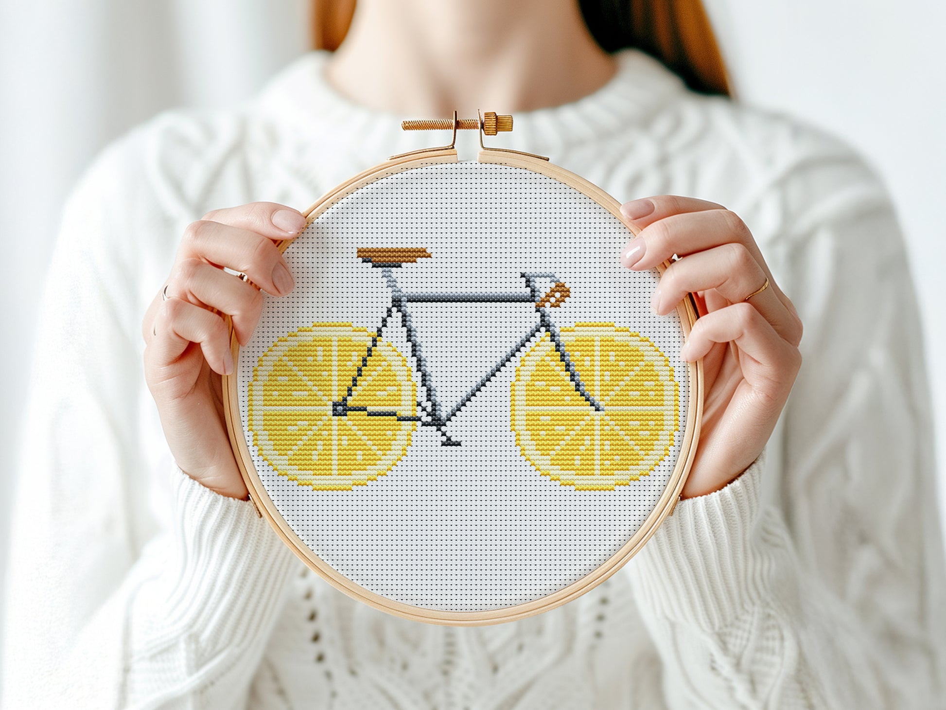 Person holding a cross-stitched bicycle design with lemon slices in an embroidery hoop.