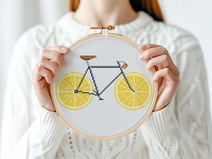 Person holding a cross-stitched bicycle design with lemon slices in an embroidery hoop.