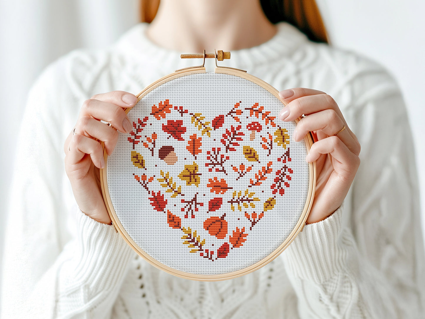 Person holding a cross-stitched heart with autumn leaves design in an embroidery hoop.