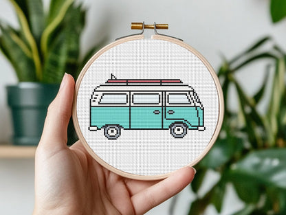 Hand holding a cross-stitched hoop with a vintage van design against a plant background