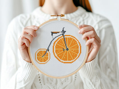 Person holding a cross-stitched bicycle design on fabric with an orange theme.