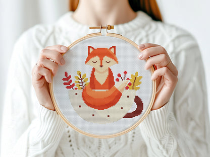 Person holding a cross-stitched hoop with a fox design against a white background