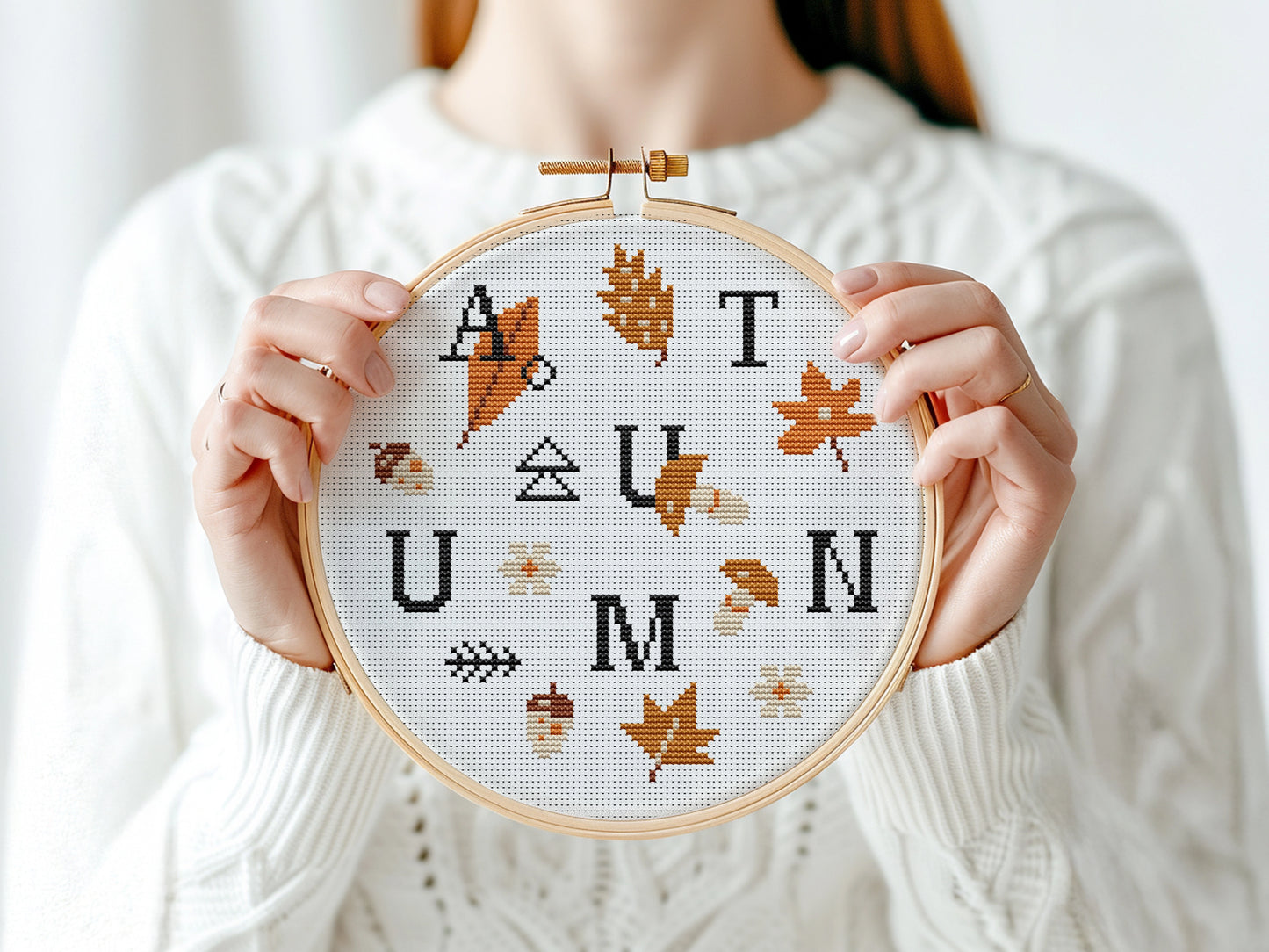 Person holding a cross-stitched hoop with 'AUTUMN' design