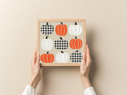 Framed art print with pumpkins and houndstooth patterns held by hands against a beige background